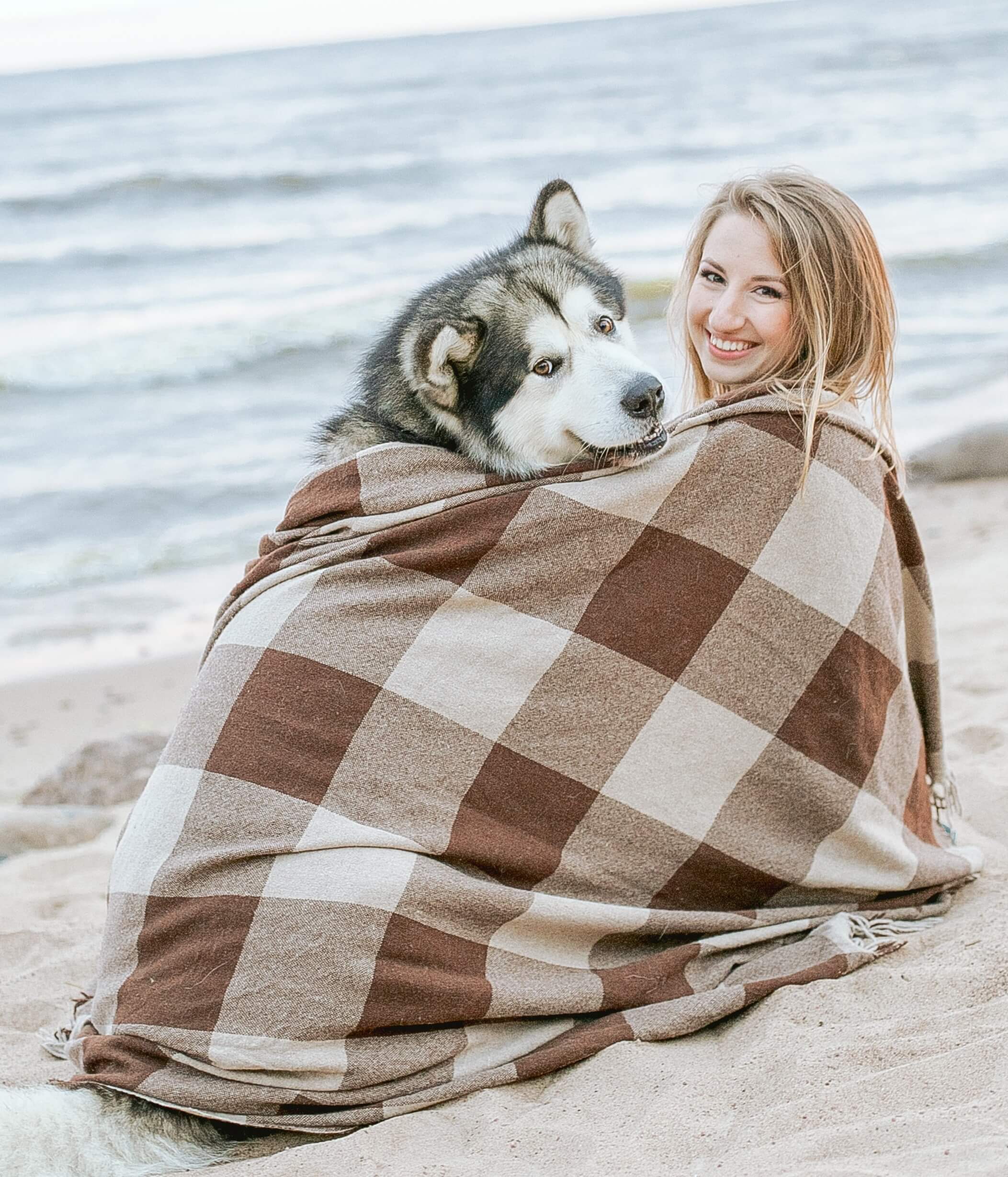 Dog and woman sitting on beach wrapped in a blanket